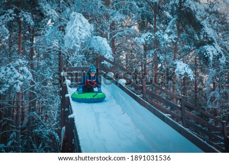 happy kid sliding on tube down snow slide in winter nature