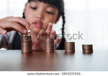 Hand of Little child girl putting coins to stack of coin step growing growth saving money, Concept finance business investment, and kid saving money for future education.             