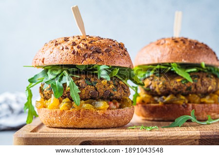 Vegan lentil burger with arugula, mustard sauce, fresh vegetables and sweet potato fries on a wooden board. Vegan food concept.