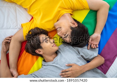 Happy Asian homosexual gay couple lying on rainbow pride flag. LGBT concept.