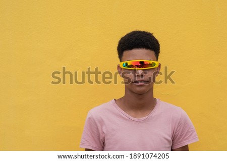Portrait of young teenager wearing cyclops sunglasses against yellow background Royalty-Free Stock Photo #1891074205