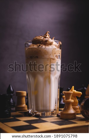 Dalgona Coffee. Whipped icing drink with instant coffee popular in Korea Creamy cocktail in tall Glasses decorated with chess on wooden chessboard