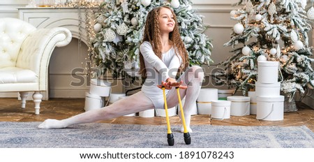 Beautiful little rhythmic gymnast performs stretching with clubs in white Christmas interior