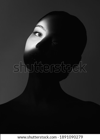 black and white portrait of beautiful girl in the dark. young woman with shadow ob the face