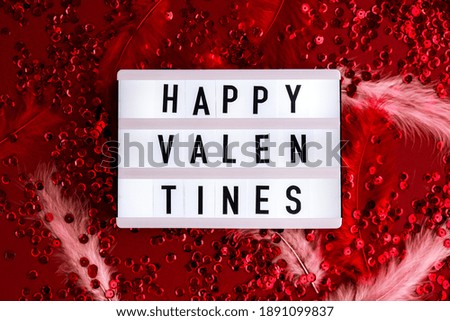 Lightbox with words for Happy Valentines on Red shiny confetti sequinned background with feathers. Saint Valentines Day and Christmas background . Holidays background and textures.