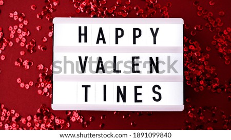 Lightbox with words for Happy Valentines on Red shiny confetti sequinned background with feathers. Saint Valentines Day and Christmas background . Holidays background and textures.