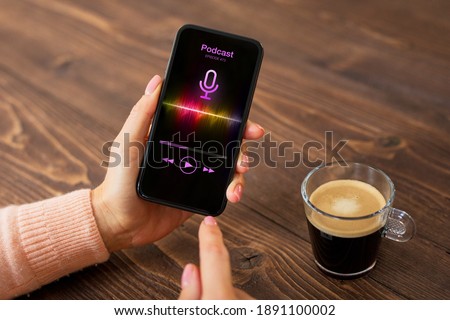 Woman having coffee and listening to podcast on her phone while Royalty-Free Stock Photo #1891100002