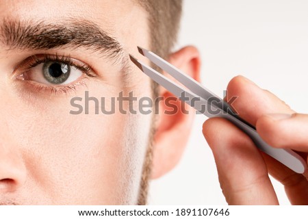 Close-up of male eye and tweezers for eyebrow grooming and shape correction Royalty-Free Stock Photo #1891107646