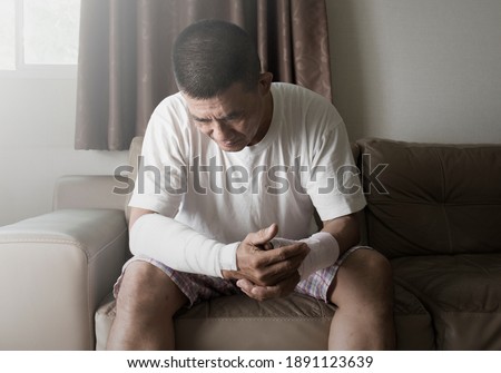 asian man suffering from mental health after an accident on the arm in home Royalty-Free Stock Photo #1891123639