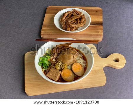 Thai-styled braised duck noodle soup with eggs, tofu and braised duck feet in white bowls on wooden serving tray