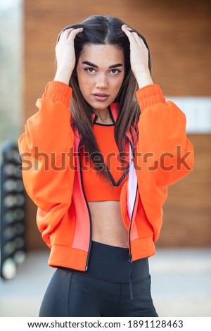 Young sporty woman in modern business district. Relaxed smiling long hair brunette fit woman in tracksuit posing and looking at camera. Young sportswoman 