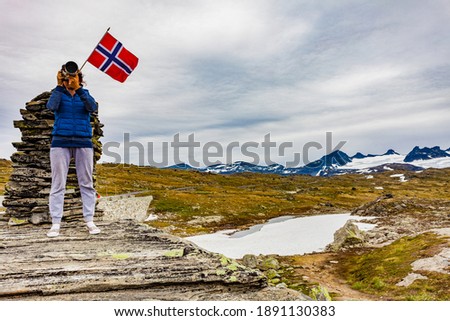 Tourist woman in mountains at high stone stack taking travel photo with camera. National tourist scenic route 55 Sognefjellet, Mefjellet viewpoint, Norway