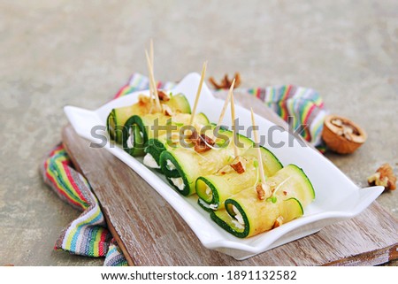 Roasted zucchini rolls stuffed with cream cheese and nuts on a white plate on a gray concrete background. Zucchini recipes. Healthy food.