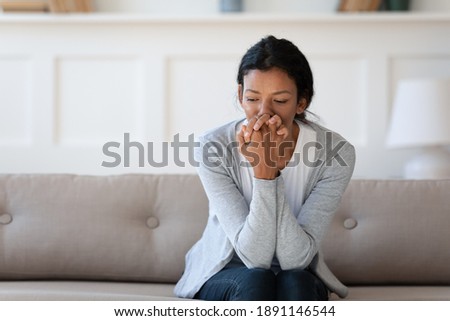 Worried young african american woman sitting on sofa, thinking of personal problems alone indoors, copy space. Unhappy mixed race lady feeling frustrated or nervous, suffering from loneliness. Royalty-Free Stock Photo #1891146544