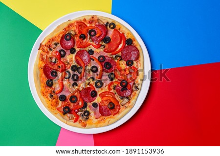 A whole, cooked and sliced peperoni pizza on a colorful backgroud, various colors. Copy space banner. Italian cuisine concept, fast food, junk food.