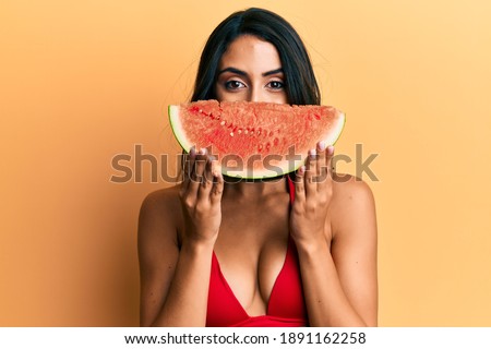Beautiful hispanic woman putting watermelon slice as funny smile smiling with a happy and cool smile on face. showing teeth. 