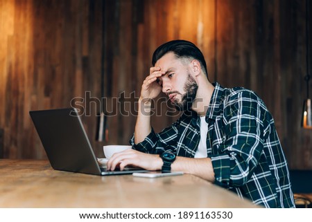 Unhappy male freelance IT professional feeling puzzled on program data code for laptop application working remotely on deadline project, tired Caucasian graphic designer watching designed video