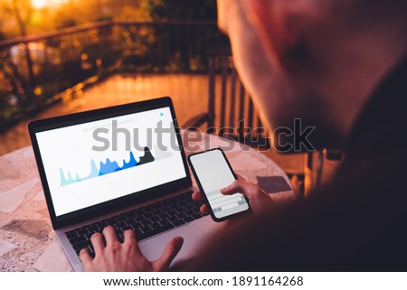 Cropped image of skilled marketer working remotely with web infographics displayed on laptop screen, business man using wireless internet connection on netbook and mobile for analyzing diagram