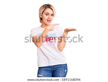 Young beautiful blonde woman wearing t shirt with diversity word message amazed and smiling to the camera while presenting with hand and pointing with finger. 