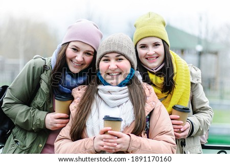 Girls in lowered face masks look at the camera and smile - Girls are having fun in the city and posing in front of the camera - Girlfriends are drinking coffee and smiling