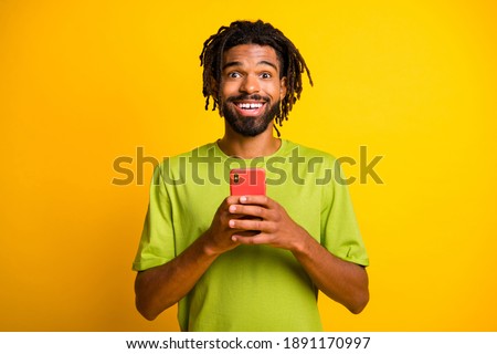 Photo of surprised dark skin guy hold smartphone like reaction concept wear green t-shirt isolated on yellow color background
