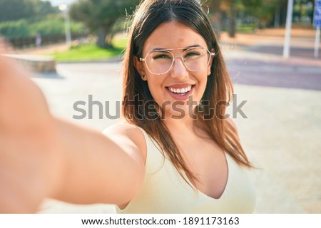 Young beautiful woman smiling happy. Standing with smile on face making selfie by the camera at town street.