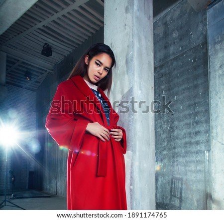 young pretty african american woman in luxury red coat posing fashionable on empty parking building, lifestyle rich people concept