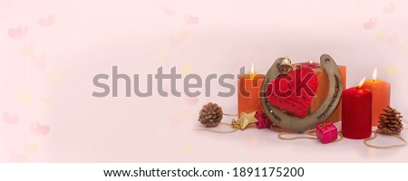 Photo poster for Valentine's Day. Shabby horseshoe for good luck, a heart made of red thread, lighted colored candles, one candle in a wooden candlestick on a pale pink background with painted hearts.