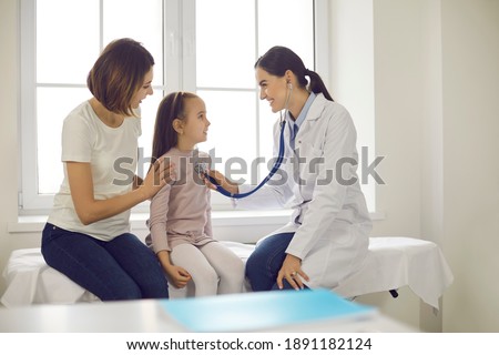 Mother and child seeing family practitioner. Smiling pediatrician with stethoscope checking little girl's lungs. Friendly doctor listening to young patient's breath or heartbeat during medical exam Royalty-Free Stock Photo #1891182124