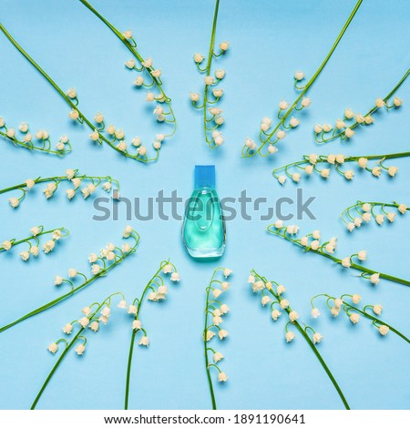 Small bottle of perfume and round frame of lilies of the valley flowers on blue pastel background. Perfumery, fragrance, cosmetic concept. Spring or summer composition. Flat lay, top view