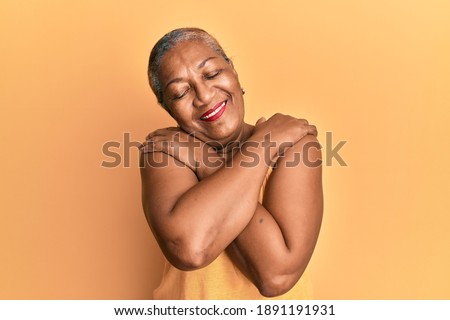 Senior african american woman wearing casual style with sleeveless shirt hugging oneself happy and positive, smiling confident. self love and self care  Royalty-Free Stock Photo #1891191931