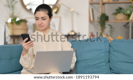 Young Indian Woman working on Smartphone and Laptop on Sofa