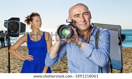 Portrait of cheerful positive male photographer with camera among professional photo equipment on seaside