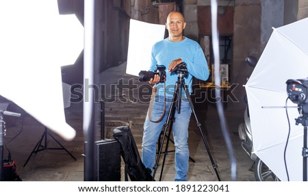 Professional photographer. Portrait of confident man holding camera in hands while standing among lighting equipment on city street