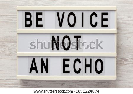 'Be voice not an echo' on a lightbox on a white wooden surface, top view. Flat lay, overhead, from above. 