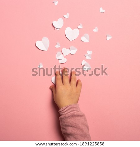Child's hand takes a valentine card from paper on a pink background. Composition Valentine's Day. Banner. Flat lay, top view.