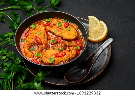 Macher Jhol in black bowl on dark slate table top. Indian cuisine Bengali Fish Curry. Asian food and meal. Royalty-Free Stock Photo #1891229332