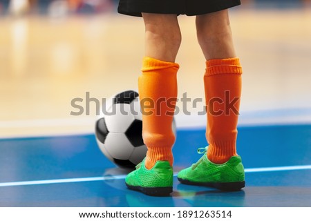 Futsal training for youth team. Young boy with soccer ball standing on white line. Indoor football soccer school practice. Kid in sportswear, black shorts, soccer cleats and orange socks Royalty-Free Stock Photo #1891263514