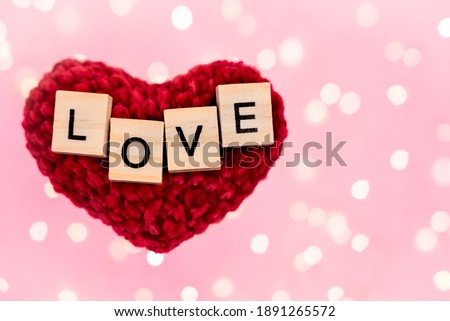 Words love on a red plush heart blurred pink background with copy-space with bokeh from a golden garland and lights. Holidays concept of mothers day, fathers day, christmas, valentines day and romance