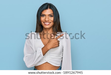 Young latin transsexual transgender woman wearing casual clothes cheerful with a smile on face pointing with hand and finger up to the side with happy and natural expression 