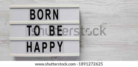 'Born to be happy' on a lightbox on a white wooden background, top view. Flat lay, overhead, from above. Copy space.
