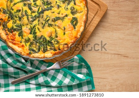 Top view on seafood and salmon fish quiche pie with baby spinach leaves- homemade recipe pie served on wooden table background with copy space. Selective focus