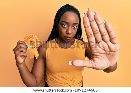 Young african american woman holding fourth place badge with open hand doing stop sign with serious and confident expression, defense gesture 