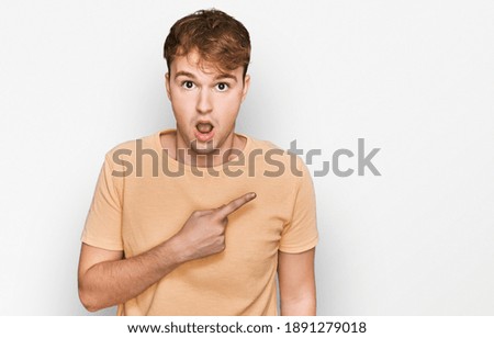 Young caucasian man wearing casual clothes surprised pointing with finger to the side, open mouth amazed expression. 