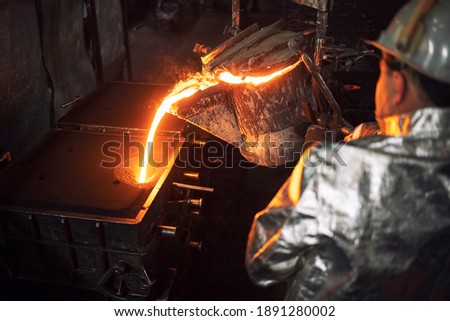 High angle view of worker filling casting molds with hot molten iron. Steel production and metallurgy. Royalty-Free Stock Photo #1891280002