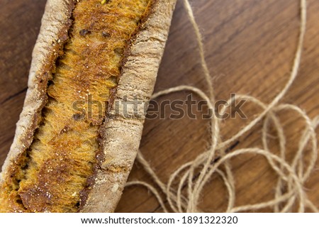 One baguette on a wooden background, with jut thread macro photography. A crispy white baguette lies on a dark textured wooden table, not all in focus. Close-up.