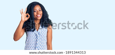 Beautiful african american woman wearing casual summer shirt smiling positive doing ok sign with hand and fingers. successful expression. 