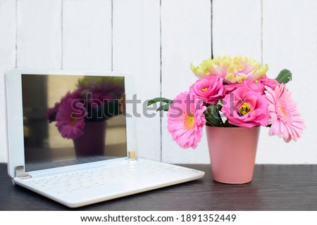 Beautiful of pink flowers in flower pot with laptop computer on black table against white wooden wall background using for your design or your concept. Stay home and work from home.