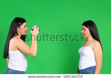 The sisters pose and take pictures with a vintage camera. Green background with empty space.
