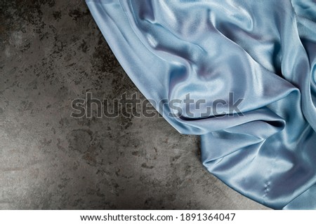 Flowing blue silk fabric on concrete background.Trend wallpaper with space for text. High quality photo